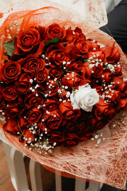 A bouquet of fresh red roses arranged with a single white rose at the center, surrounded by sprigs of delicate white baby's breath flowers. The roses are tightly clustered and appear vibrant and velve